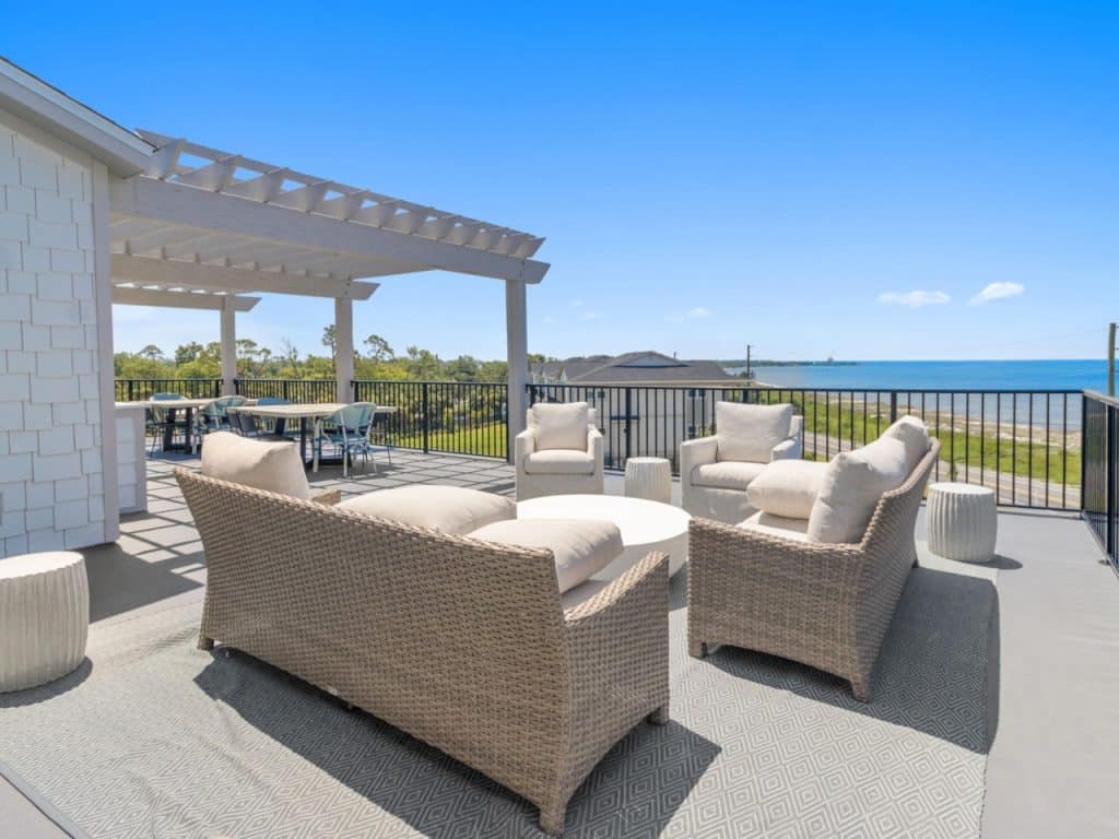 coastal designed second story patio overlooking the water with beachy white patio furniture and accessories designed and decorated by Shore House Furniture in Panama City Beach Florida