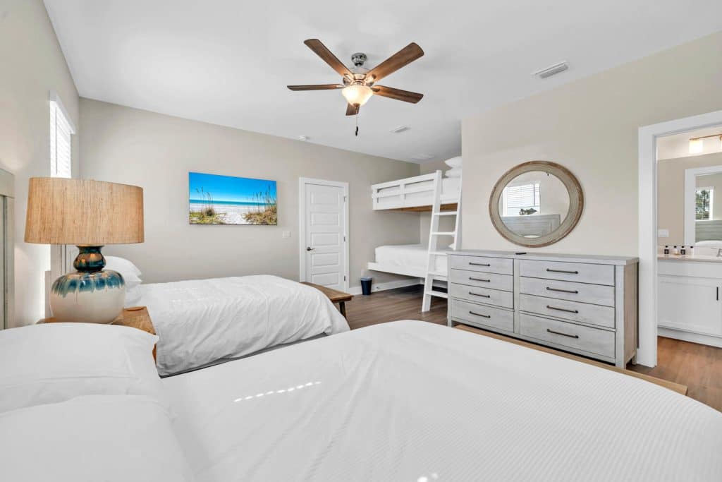 coastal designed guest bedroom with two queen beds and a bunk bed with beachy white accessories designed and decorated by Shore House Furniture in Panama City Beach Florida