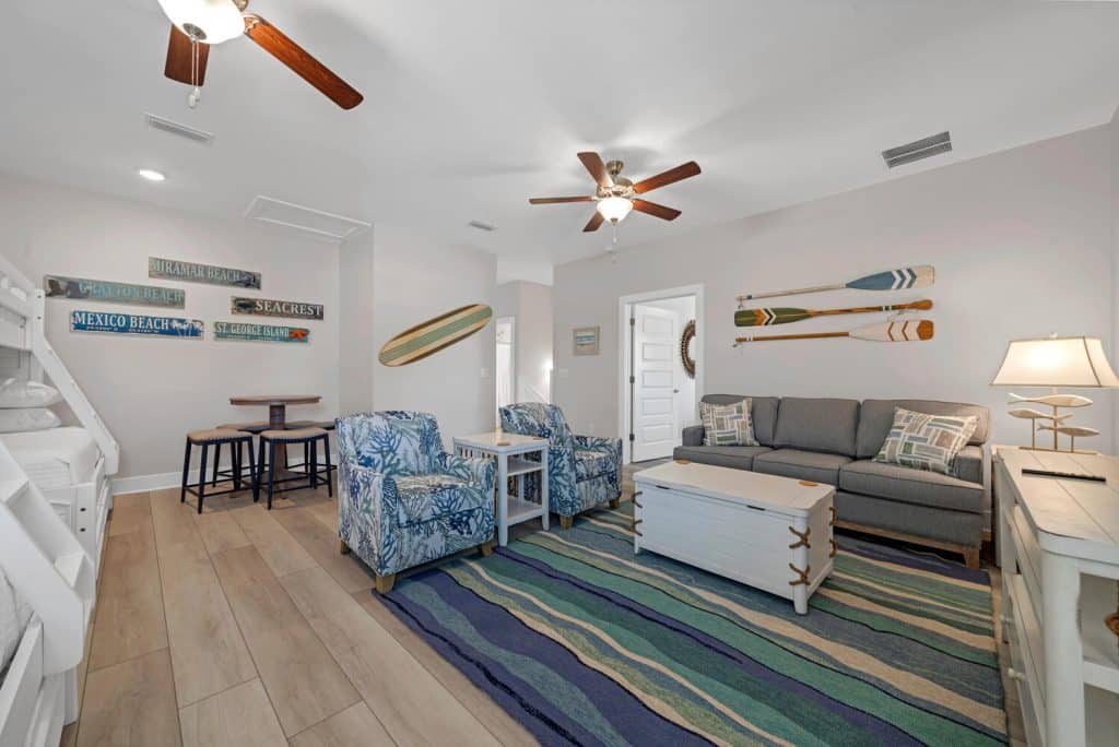 coastal designed guest bedroom with 2 sets of bunkbeds couches and chairs with beachy white and teal accessories designed and decorated by Shore House Furniture in Panama City Beach Florida