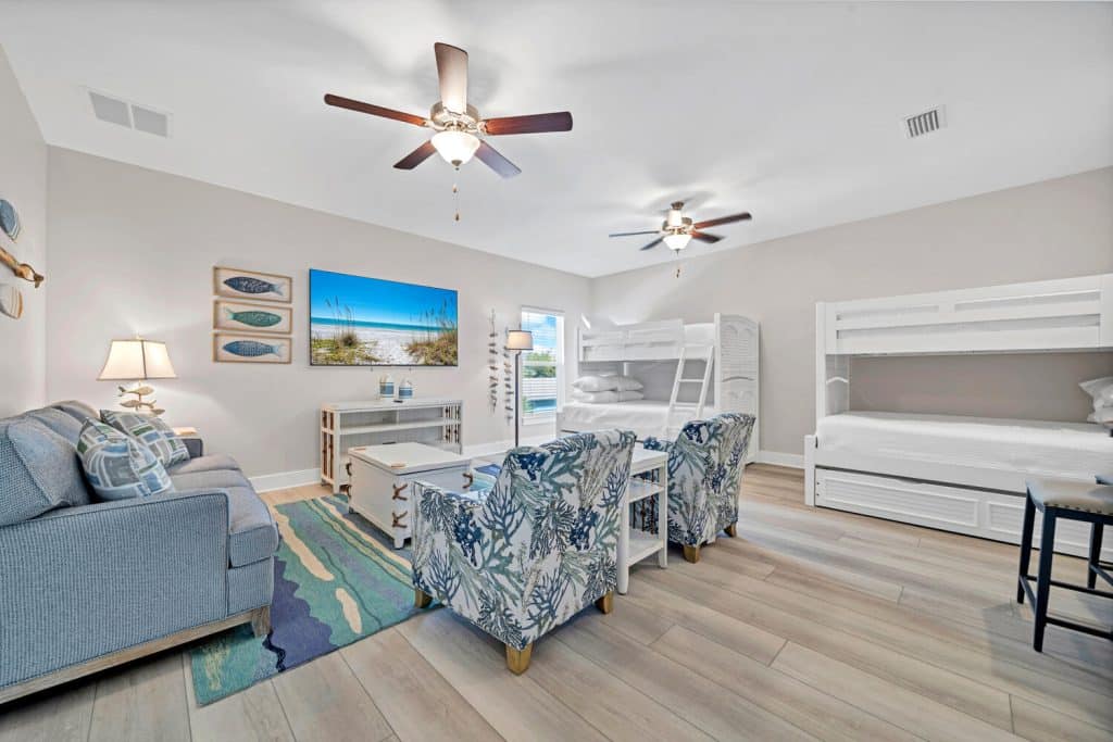 coastal designed guest bedroom with 2 sets of bunkbeds couches and chairs with beachy white and teal accessories designed and decorated by Shore House Furniture in Panama City Beach Florida